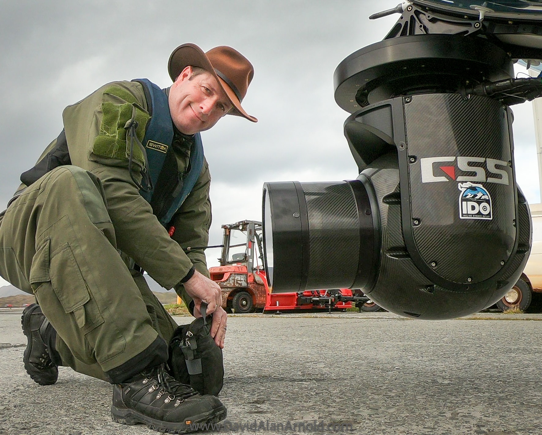 David Alan Arnold crouching next to a gyro-stabilized camera pod mounted on the aircraft