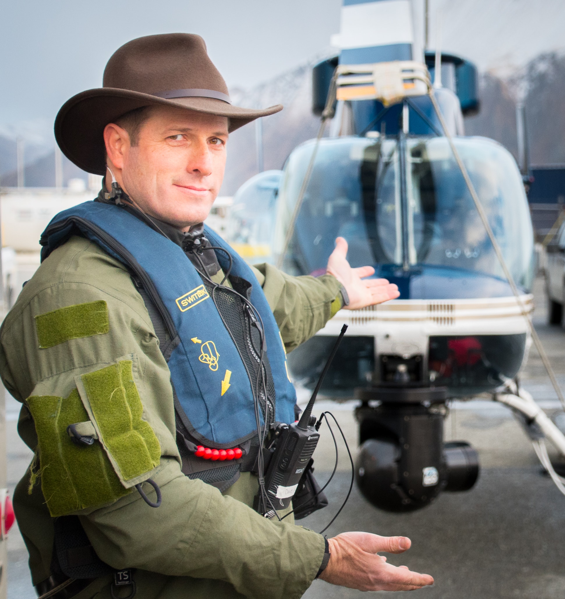 David Alan Arnold in survival vest gesturing toward helicopter with camera pod, Deadliest Catch