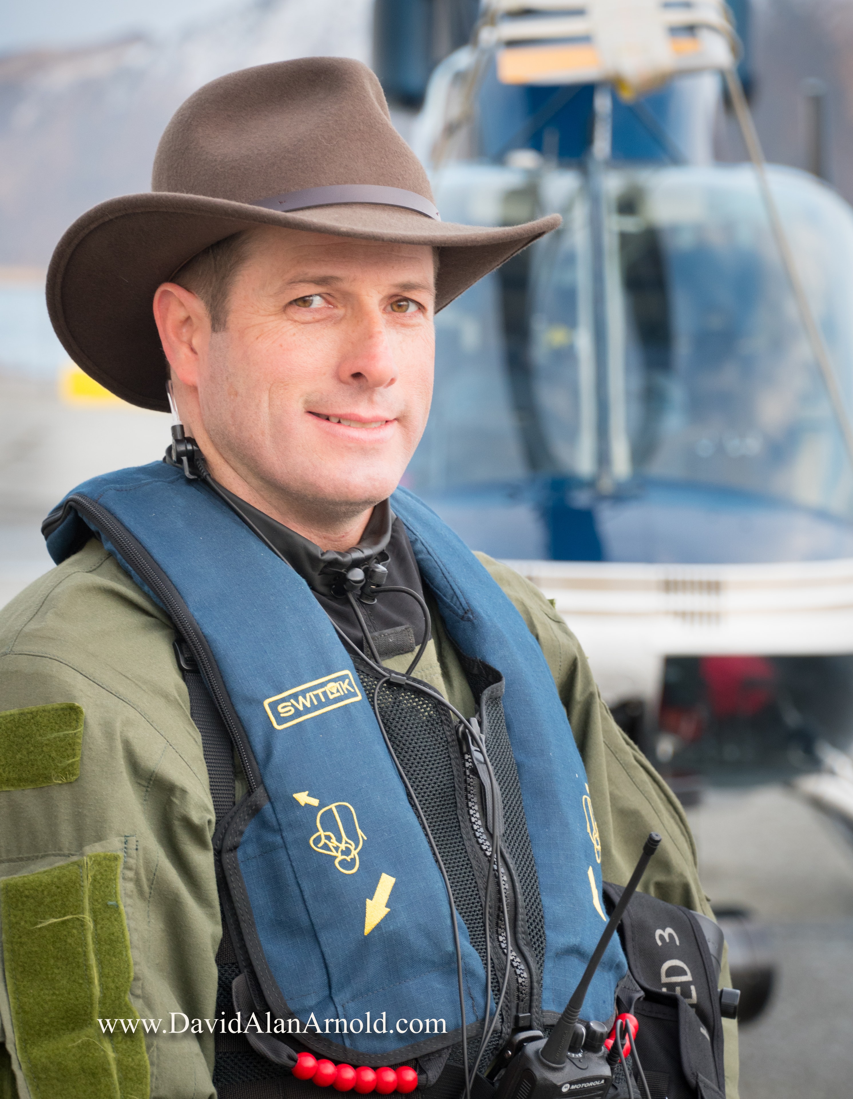 Portrait of David Alan Arnold in cowboy hat and survival gear with helicopter behind him, Deadliest Catch Discovery