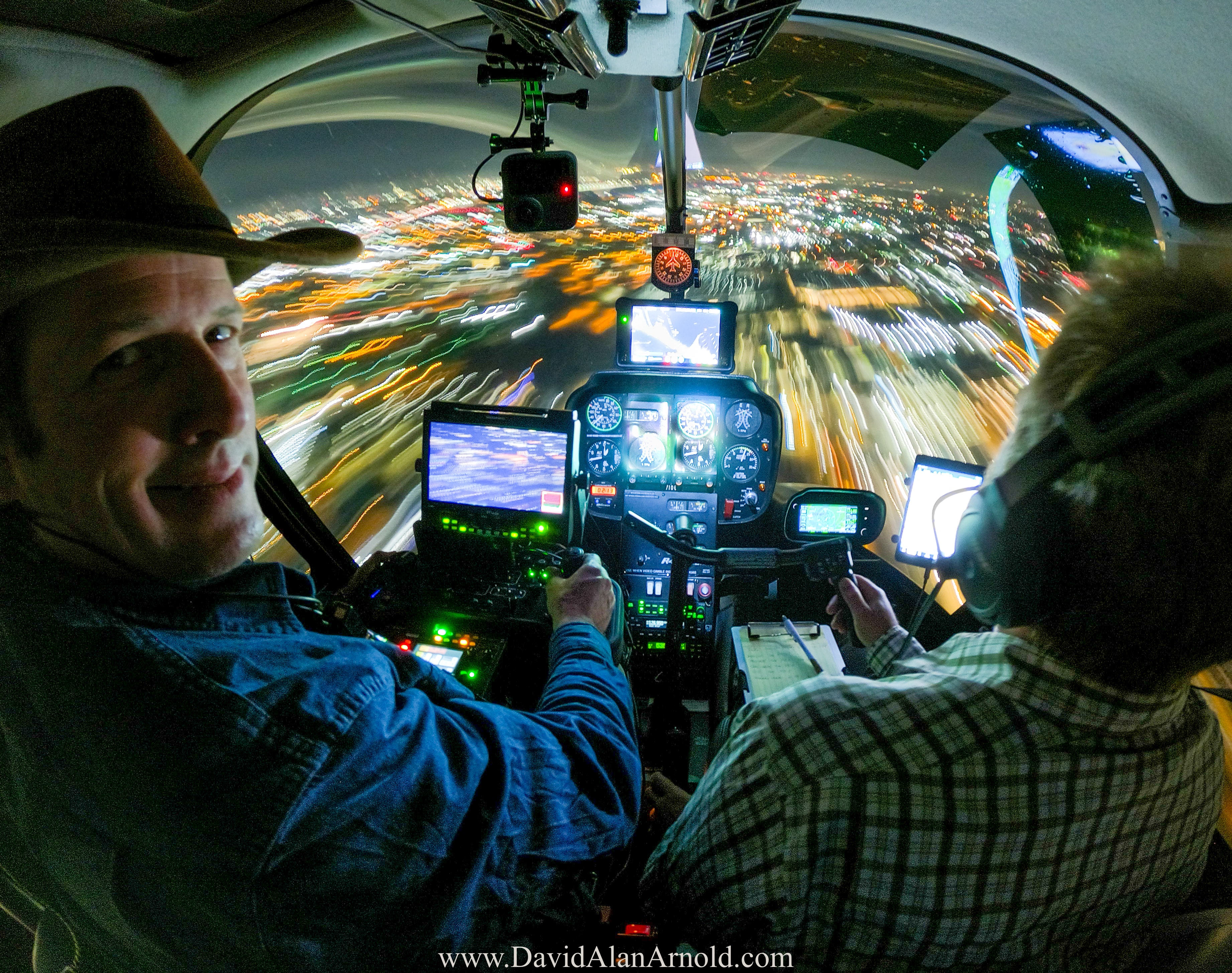 David Alan Arnold smiling at camera in helicopter cockpit, city lights streaking below at night, Monday Night Football