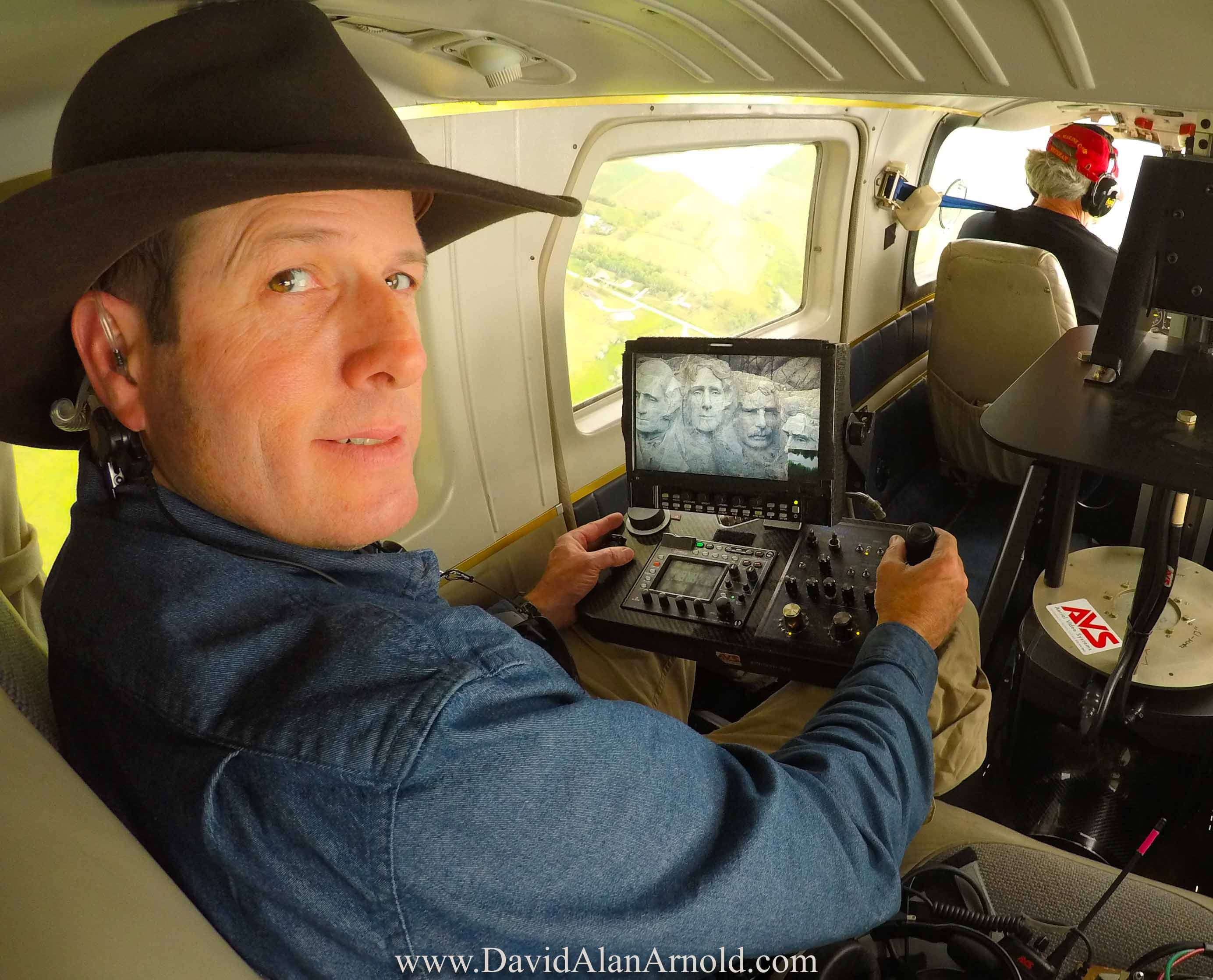David Alan Arnold operating camera controls in aircraft with Mount Rushmore on the monitor