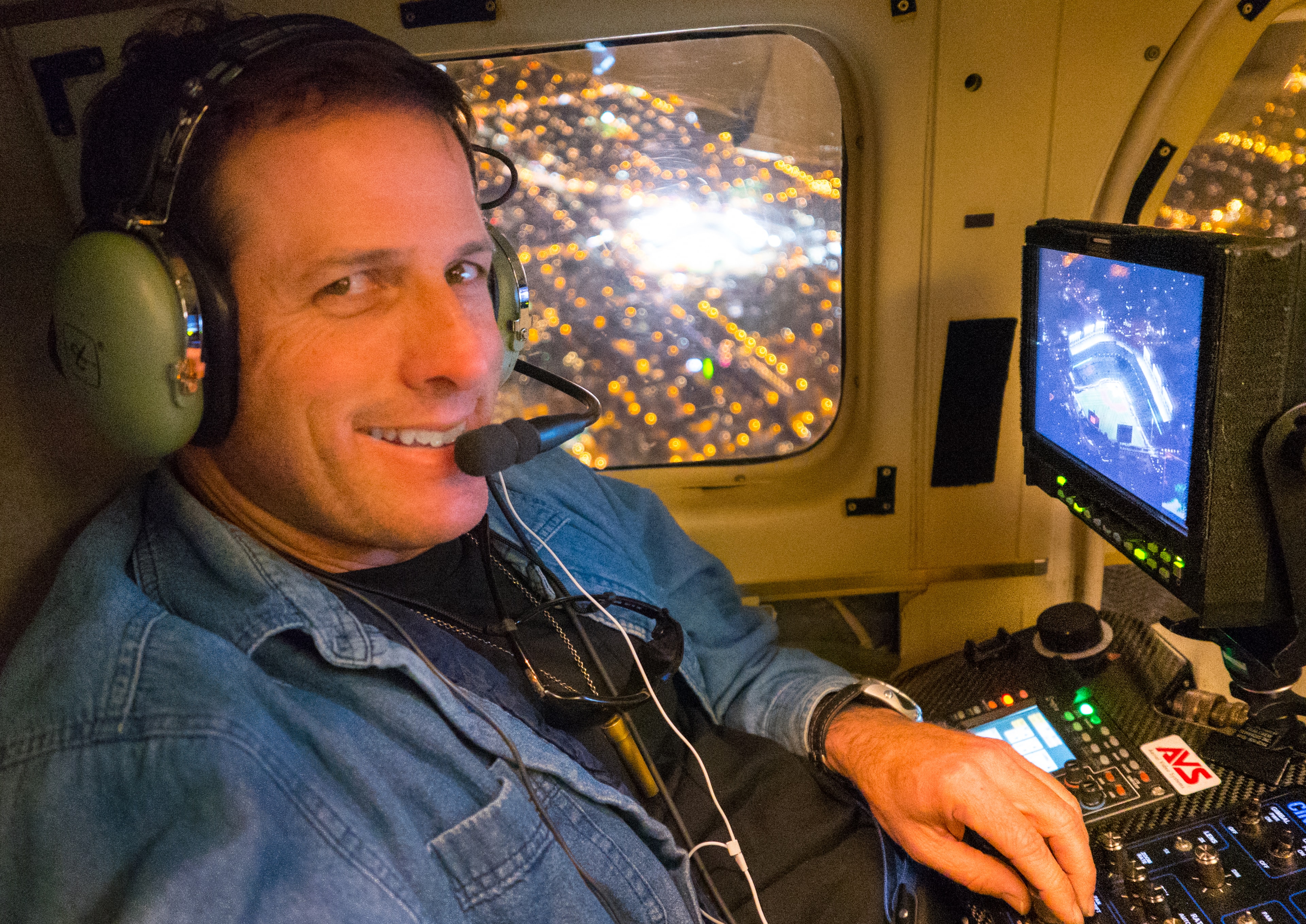 David Alan Arnold smiling in helicopter cockpit at night, city lights below and stadium on monitor, Chicago World Series